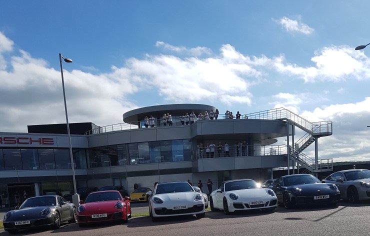 [Muscle Warrior team standing on a viewing platform looking down at a carpark filled with Porsche's]